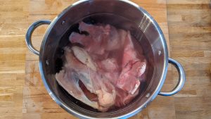 os de porc carcasses de poulet et pied de porc découpés en disques dans une grande marmite remplie d'eau